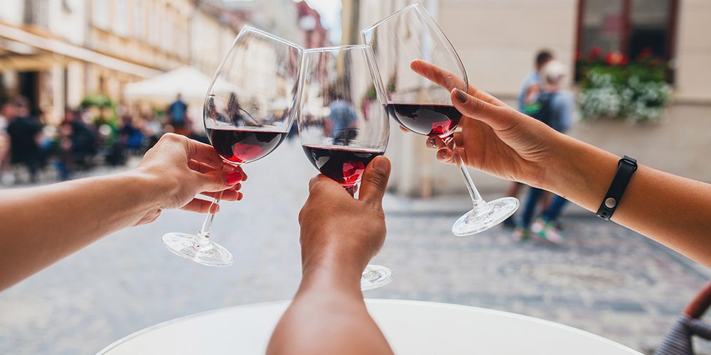 Come bevono le nuove generazioni? Un articolo di Alessandro Rossi. In foto, tre braccia avvicinano i calici con vino rosso in un brindisi