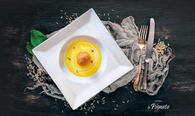 Arancino di risotto ai porcini e salsiccia con cuore di pecorino carmasciano, panatura di mais e quinoa, su vellutata di zafferano e tartufo nero