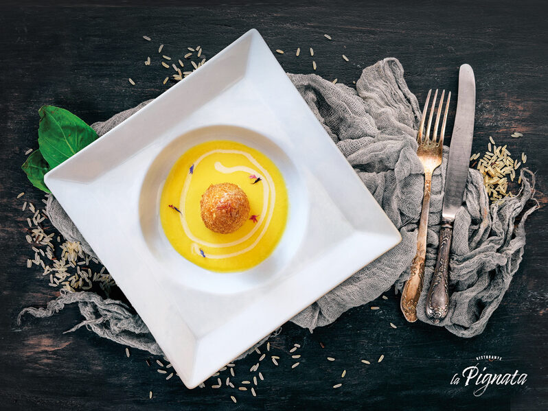 Arancino di risotto ai porcini e salsiccia con cuore di pecorino carmasciano, panatura di mais e quinoa, su vellutata di zafferano e tartufo nero
